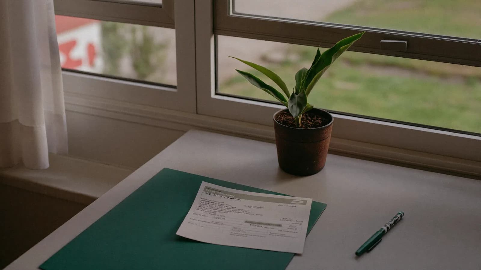 Escritorio junto a una ventana con documentación bancaria y una planta